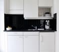 modern kitchen with white cabinets, black tiled countertop, integrated sink, stainless steel faucet, espresso machine, refrigerator