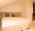 spacious bedroom with beige upholstered bed, white bedding, two brown pillows, beige nightstand, large white wardrobes, and adjacent bathroom with walk-in shower and marble floor