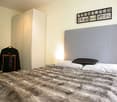 A bedroom with a large bed and fur comforter, a wardrobe, and an empty wall space.
