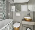 modern bathroom, large mirror, round golden sink, white ceramic toilet, bathtub, patterned walls, large shower