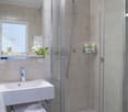 A modern bathroom with a white vanity, shower enclosure, and tiled walls.