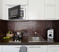 modern kitchen, white cabinets, brown tiled backsplash, stainless steel sink, gas stove, microwave, coffee machine, black countertop