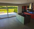 Modern kitchen with a large island, black countertops, green cabinets, and a sliding door leading to a patio.