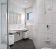 modern bathroom with white tiles, glass shower enclosure, white sink, white cabinets, toilet, window with blinds
