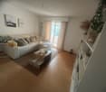 Living room, white sofa, coffee table, rug, white shelving unit, two picture frames, sliding glass door leading to balcony, plants