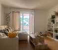large windows, sliding glass door to balcony, beige couch, coffee table, open bookshelves