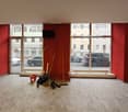 empty room with red walls, tiled floor, 3 large windows, equipment and cleaning products scattered on the floor