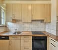Spacious kitchen with light wood cabinets, tile backsplash, stainless steel sink, and built-in dishwasher and oven