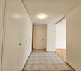 Empty hallway with tile flooring, white walls, cabinets, closed white door, and recessed ceiling light