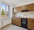 Spacious kitchen with wooden cabinets, tiled backsplash, electric stove, and dishwasher. Large windows provide natural light and a view of the outdoors.