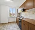 Spacious kitchen with wooden cabinets, tiled backsplash, electric stove, and a dishwasher. Large window providing natural light and a view of the surrounding area.