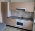 The image shows a kitchen with beige cabinets, a tiled backsplash, a white stove, and a dishwasher. The floor is tiled with a light-colored tile.