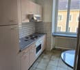 Compact kitchen with light-colored cabinets, tiled backsplash, and a dishwasher. The kitchen has a window overlooking the exterior buildings.