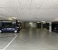 Underground parking garage with concrete floor, parked cars, and storage rooms