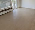 This image shows an empty room with a large window and tile flooring. The walls are painted a light color and there are wooden beams on the ceiling. The room appears to be a living room or bedroom based on the size and layout.