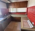 The image shows a kitchen with wooden cabinets, red tile backsplash, and a dishwasher visible on the counter. The floor appears to be a light-colored wood or tile. The kitchen has a modern, retro-inspired design aesthetic.