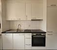 The image shows a modern kitchen with white cabinets, a black countertop, a stainless steel sink, and a built-in oven and cooktop. There is also a dishwasher visible in the kitchen.