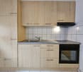 The image shows a modern kitchen with light wood cabinets, a stainless steel sink, a built-in oven, and a dishwasher.
