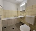 Tiled bathroom with bathtub, sink, and toilet. The walls are covered in beige tiles and there is a mirrored cabinet above the sink.