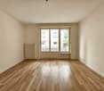 Spacious living room with hardwood floors, large windows, and a radiator. The room appears to be empty, ready for furnishing and decorating.