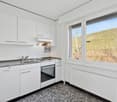 Bright and modern kitchen with white cabinets, stainless steel appliances, and a large window overlooking a scenic outdoor landscape.