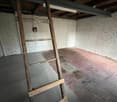 Unfinished basement or storage room with exposed brick walls, wooden beams, and a wooden ladder leaning against the wall.