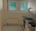 Tiled floor, white walls, windows with green blinds, kitchen counter with sink and dishwasher