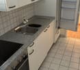 Compact kitchen with white cabinets, granite countertop, stainless steel sink, built-in dishwasher, and a refrigerator. The floor is tiled with a neutral color scheme.