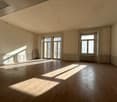 Large, open room with hardwood floors, white walls, and large windows allowing natural light to flood the space. The room appears to be empty, with no furniture or decor visible.