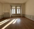 Spacious room with hardwood floors, large windows, and paneled walls. The room appears to be empty, with natural light streaming in through the windows.