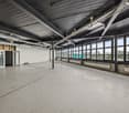 Large open commercial space with high ceilings, exposed metal beams, and large windows providing a view of the surrounding area. The space appears to be unfinished or under renovation, with a concrete floor and minimal furnishings.