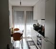 modern kitchen with wooden dining table, two chairs, white cupboards, tiled floor, glass doors leading to balcony, gas stove, oven