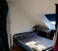 small single bed, bed sheets and pillows, table with lamp, clothes hanging from rack