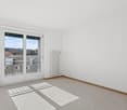 Empty room with sliding glass doors, balcony with railings, white walls, white ceiling, and radiator.