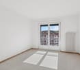 White walls, sliding glass doors leading to balcony, carpet floor, white radiator