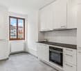 modern white kitchen, dishwasher, built-in oven, tiled floor, white cabinets, black granite countertop, radiator