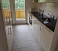 modern kitchen, white cabinets, black countertops, stainless steel sink, gas stove, integrated oven, white tiled flooring