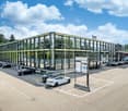 Glass-fronted building, several cars parked, large entrance