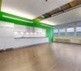 empty room with kitchen, wooden floor, white walls, green wall, white cabinets, windows, built-in oven, sink, faucet, radiator