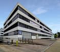 modern office building, concrete exterior, glass windows, multiple floors, parking area, entrance ramp