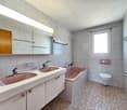 Bathroom with two sinks, bathtub, toilet, mirror, and tiled floor.