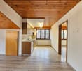 An empty kitchen with wooden cabinets, tiled floor, wooden ceiling, and a sink with faucet.