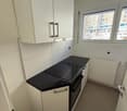 modern kitchen with white cabinets, black countertop, electric stove, integrated dishwasher, white floor, window