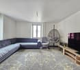 Large living room with grey velvet sofa, light walls, modern design floor lamp, hanging chair, TV, and white tile floor.
