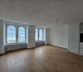 large room, wooden floors, three large windows, white walls, white cabinets, radiators under windows
