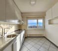 Modern white kitchen with sink, oven, tiled floor, and window with a city view