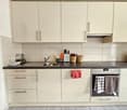Modern white kitchen with countertops, a sink, and a stove. It has cabinets and drawers for storage and a dishwasher underneath the countertop.