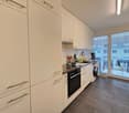 modern kitchen with white cabinets, wooden floor, black appliances, washing machine, dishwasher, large windows