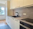 modern kitchen with white cabinets, gray countertops, black sink, black faucet, built-in oven, induction stove, and a window with a view of trees
