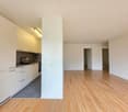 Empty kitchen with white cabinets, wooden floor, gray tiles, sink, faucet, and a power outlet
